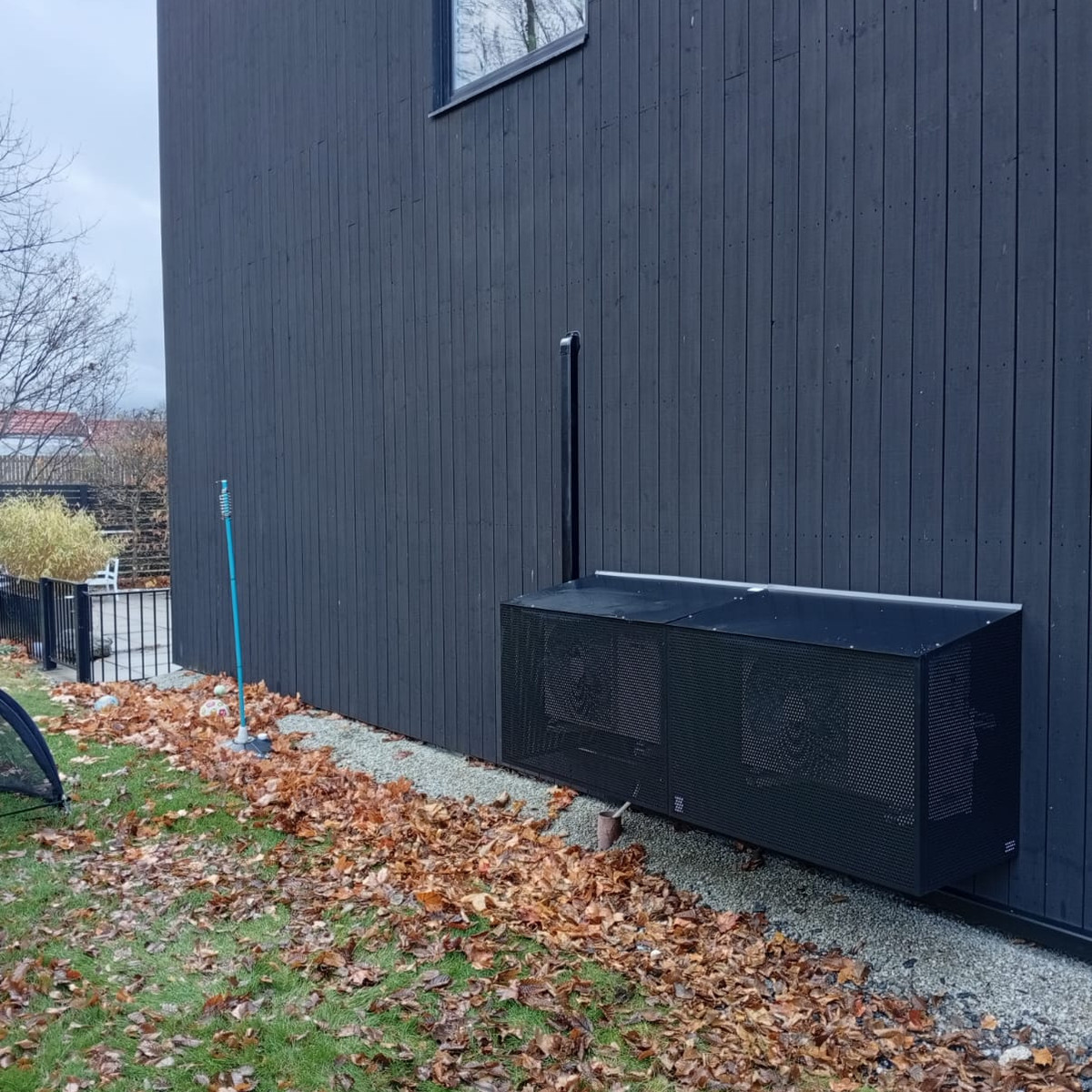 Svarta plåtskydd till luftvärmepumpar på svart träpanel